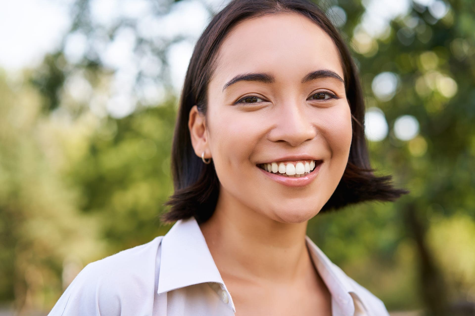 Portrait souriant d'une jeune femme en chemise blanche, dans un parc