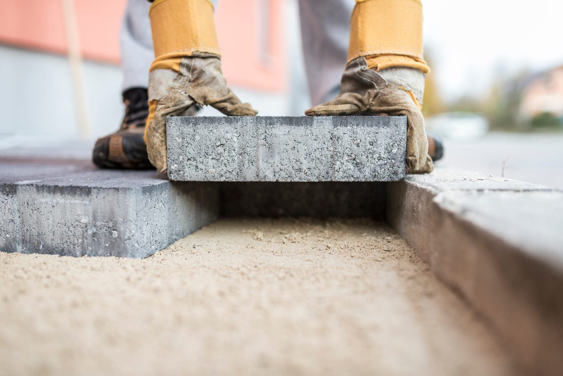 Pose d'un pavé de béton gris sur un lit de sable nivelé, mains gantées